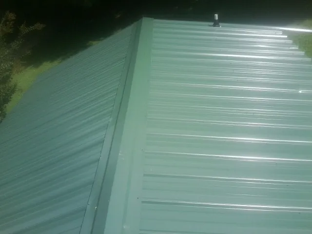 New green metal panels meeting at the ridge of a roof — Flat Roof Repair work by our crew in Palatka