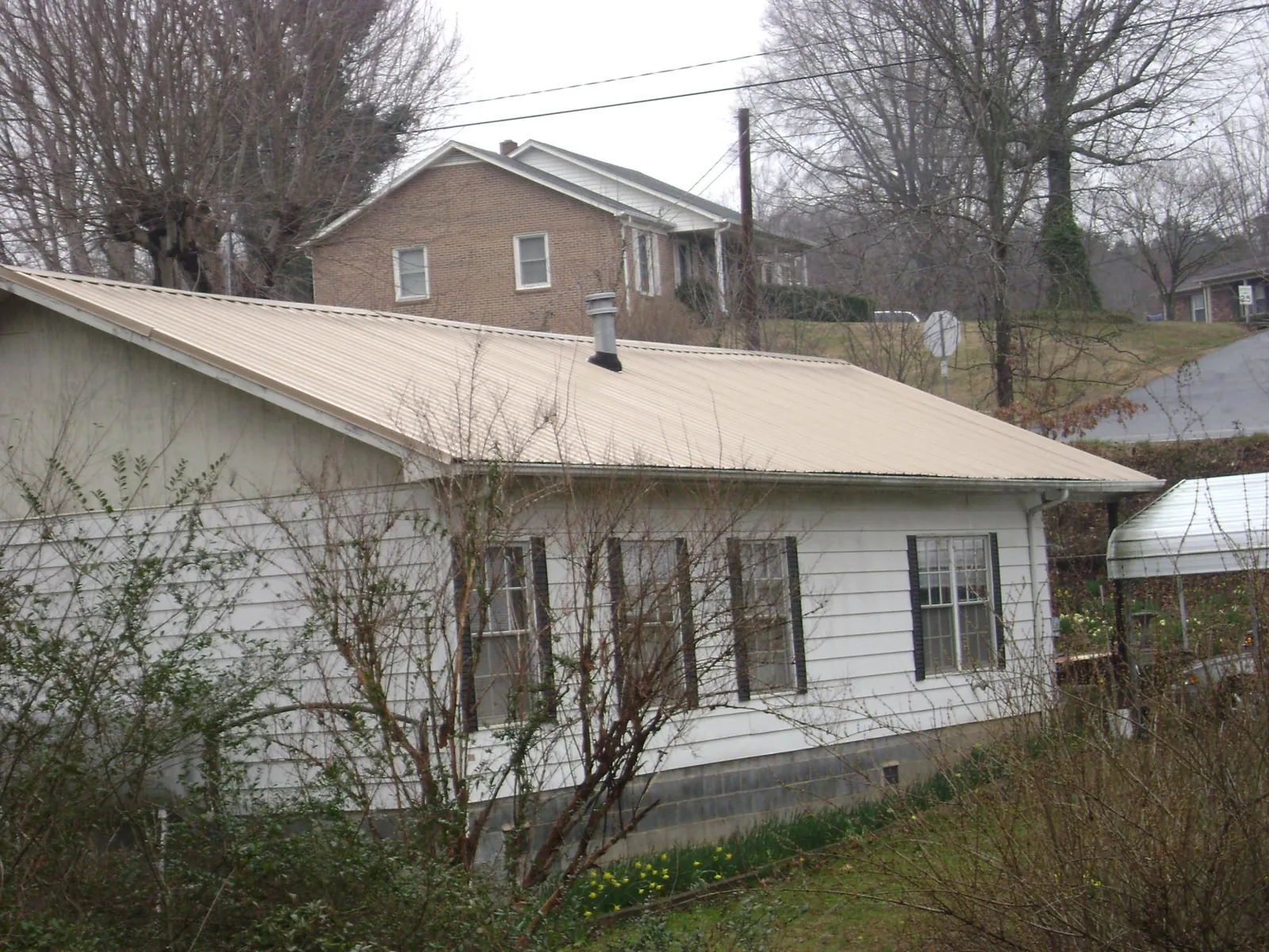 Tan metal roof on a white sided house set into a hillside — Commercial Roofing by Roofing Brothers in Palatka
