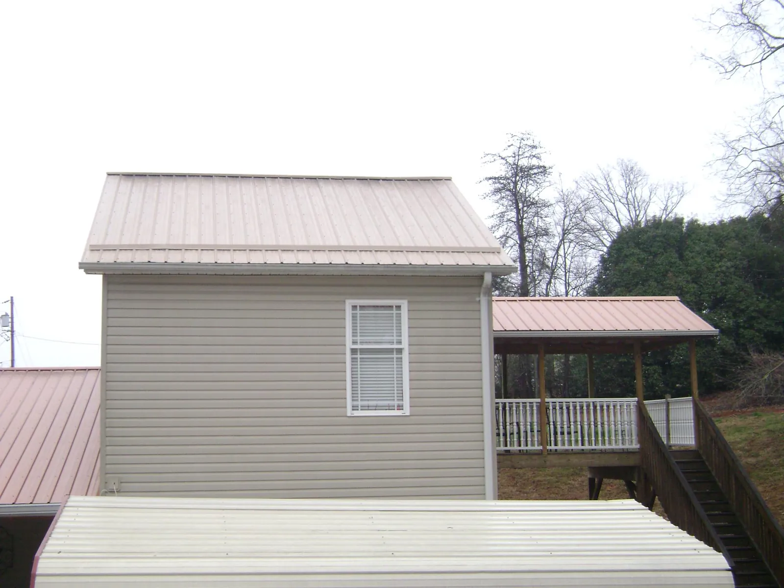 Tan metal roofs on a two story addition and attached porch, from a Roof Replacement job in Palatka